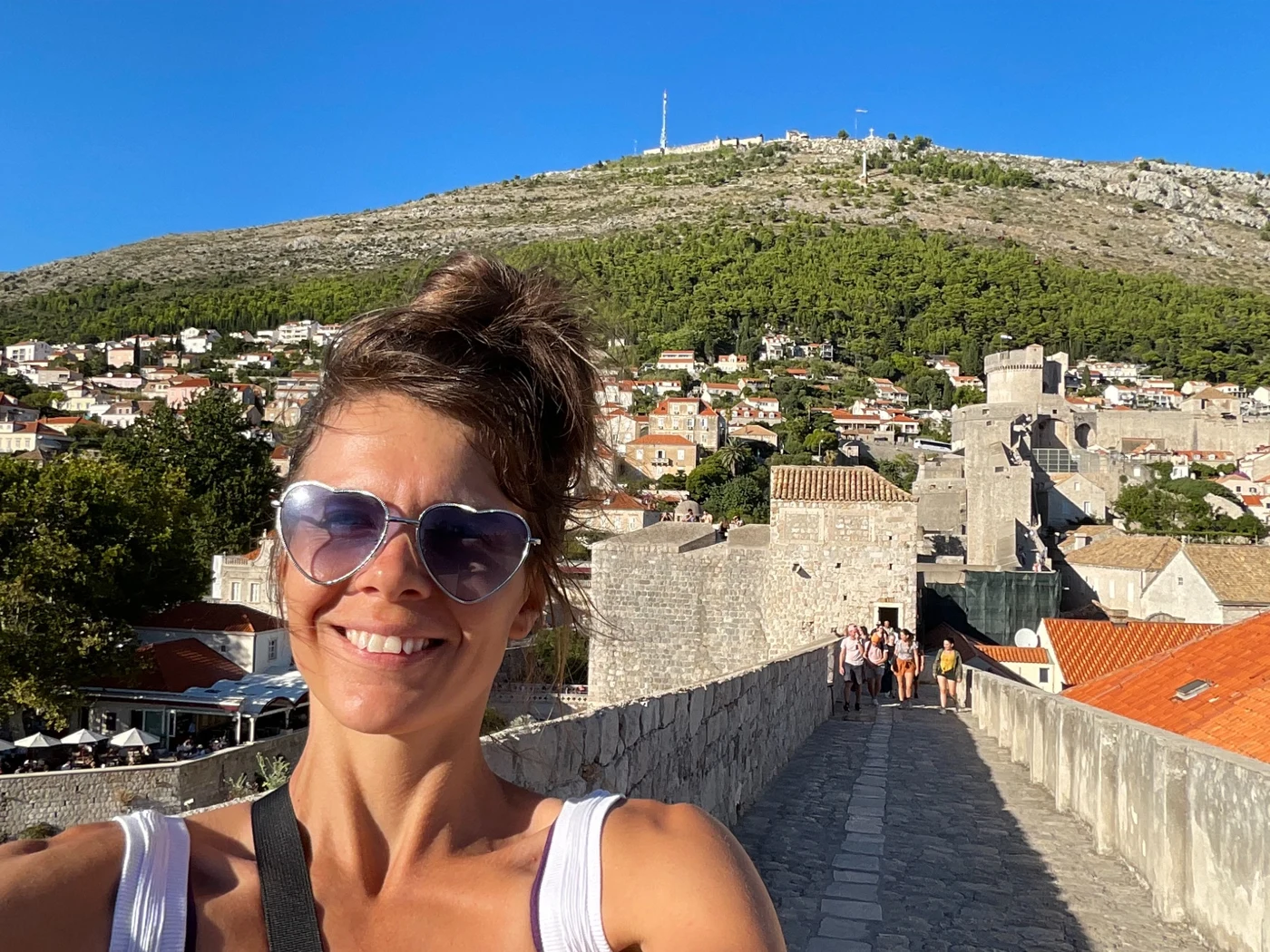 Rozzebud smiling in heart-shaped sunglasses while exploring historic stone city walls beneath a blue sky